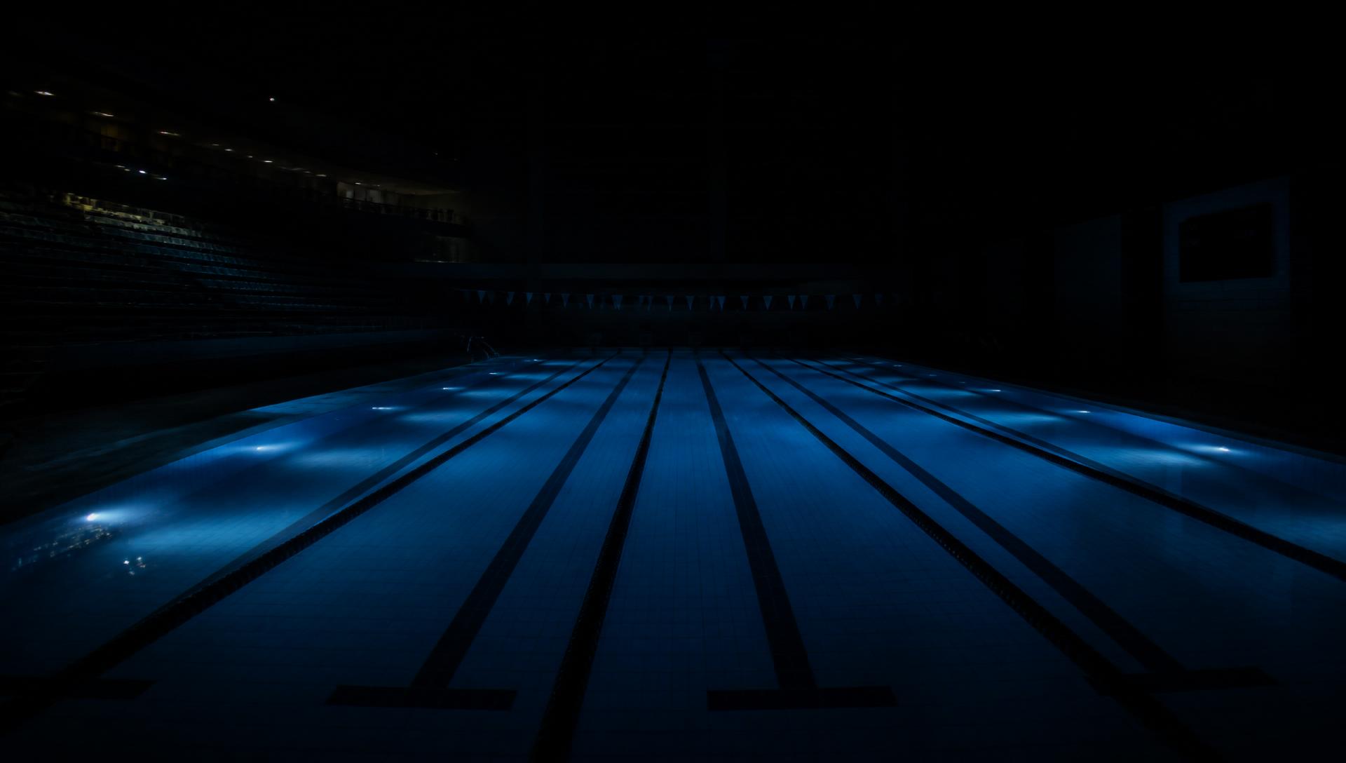 Empty Olympic pool at night, underwater lights on